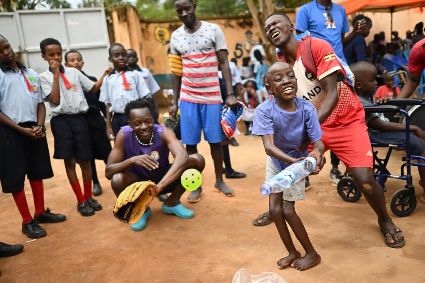 Gayaza, Uganda April 1, 2023-Dennis Kasumba teaches a disabled child to play baseball at St. Lilian Jubilee Home in Guyaza, Uganda. Some of the players along with their coach travel to the church-run home for disabled and disadvantaged children at least once a week. (Wally Skalij/Los Angeles Times)