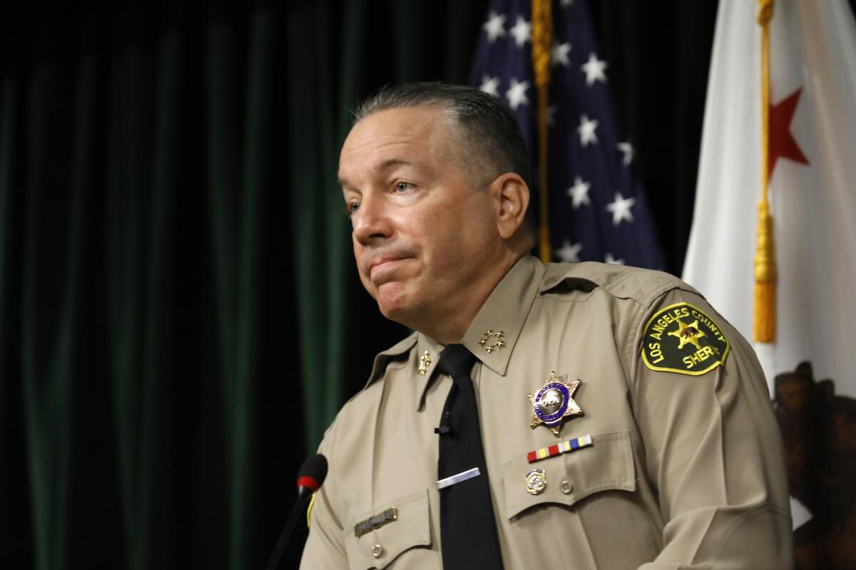 A man in uniform stands in front of an American flag and a California flag.