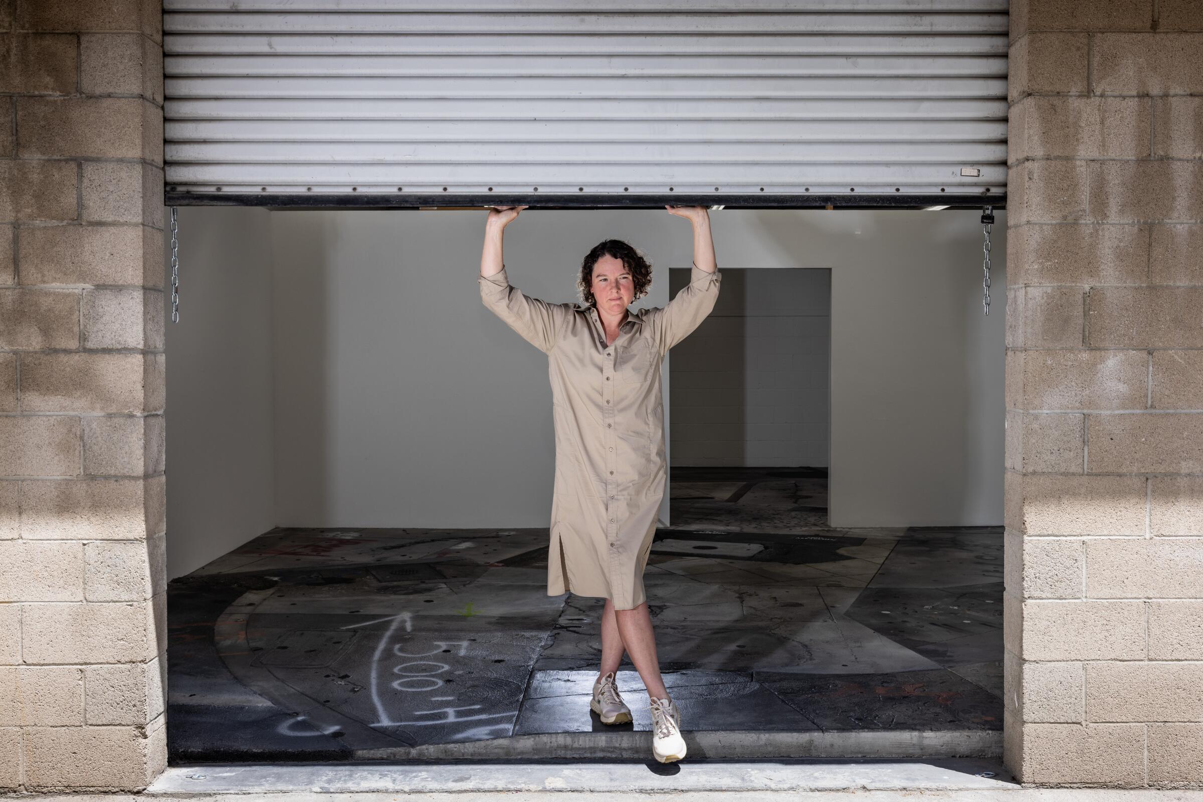A woman stands with her arms up as if holding up the roll-up garage door over her head.