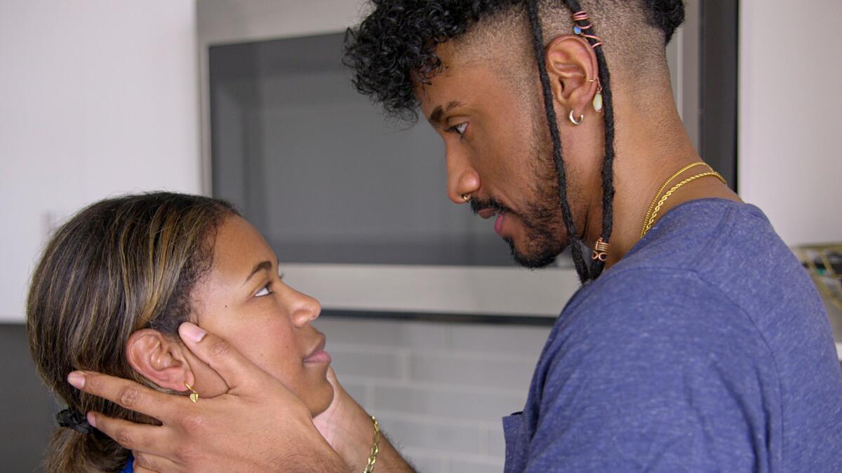 A woman looks up at a man who is holding her face in his hands.