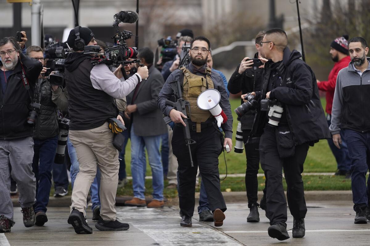 A man surrounded by photographers carries a rifle.