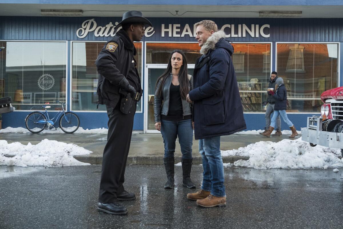 Corey Reynolds, Sara Tomko and Alan Tudyk stand outside a health clinic in Syfy's "Resident Alien."