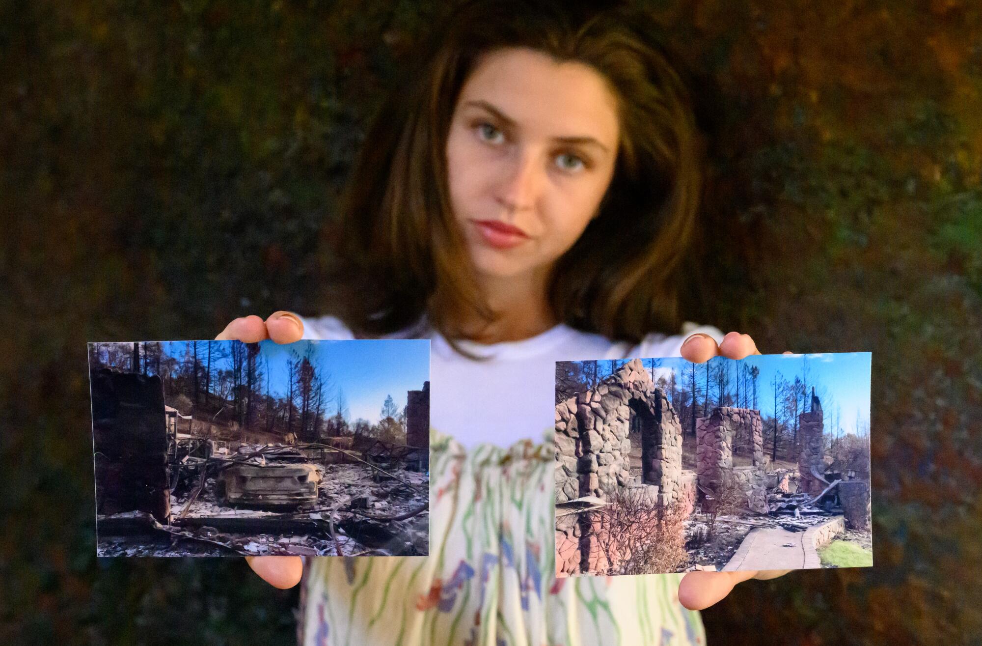 A young woman holds photos of a  fire-gutted home in each hand.