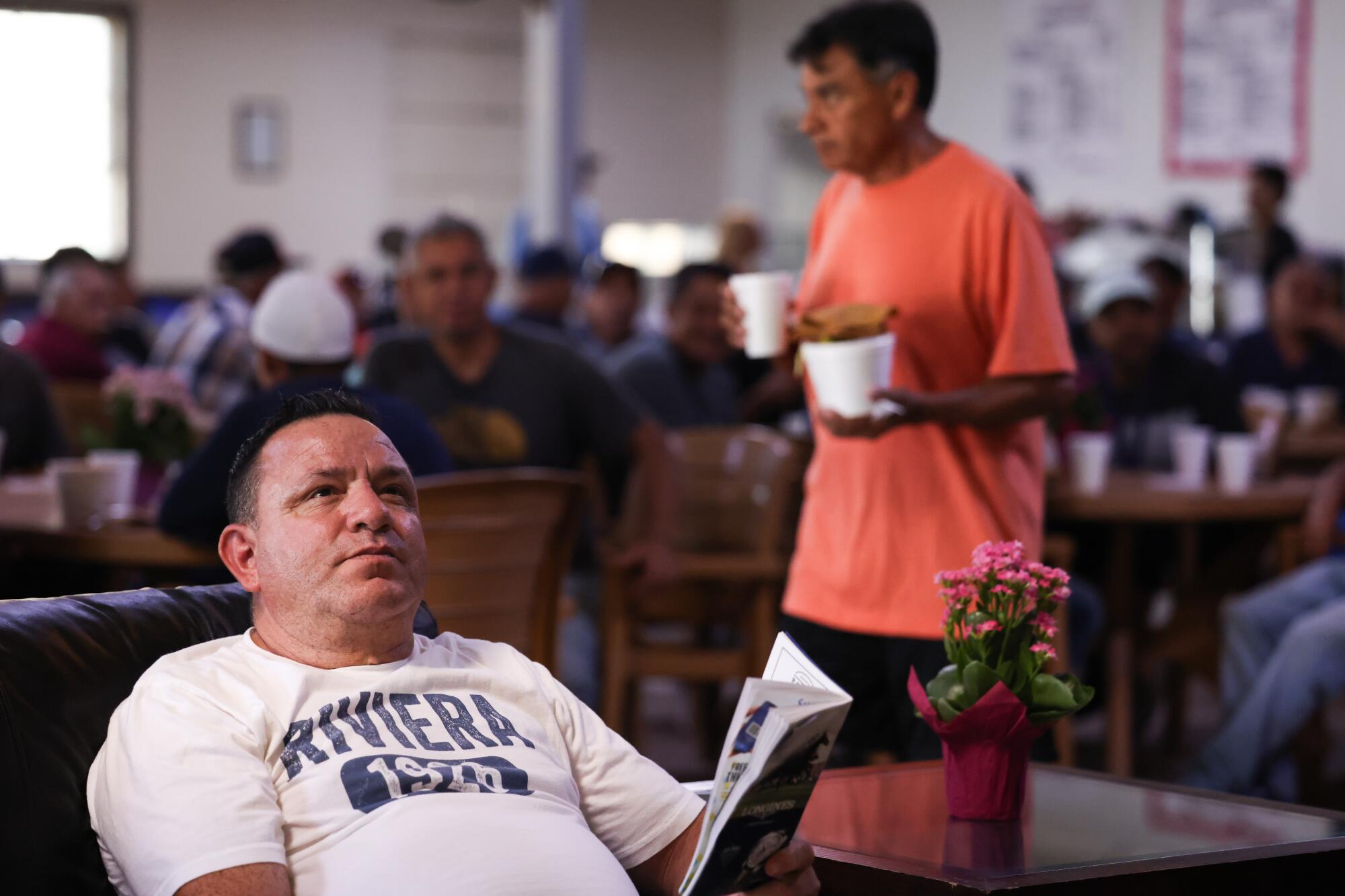Rudy Cruz, an assistant foreman for trainer Phil D'Amato, left, watches a race as others eat their meals.