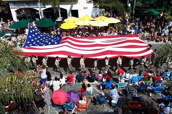 Scouts carrying a huge American flag march along a packed Main Street during the 107th annual Fourth of July parade of Huntington Beach.