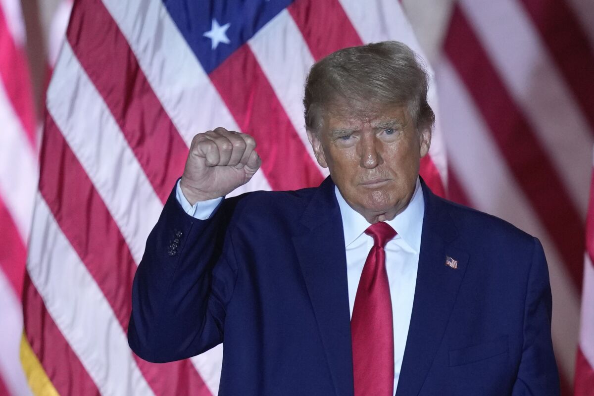Former President Trump standing in front of a large American flag, raising his fist