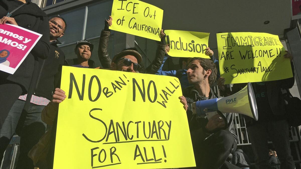 Protesters in 2017 hold up signs outside a San Francisco courthouse where a judge heard arguments in the first lawsuit challenging President Trump's executive order to withhold funding from communities that limit cooperation with immigration authorities.