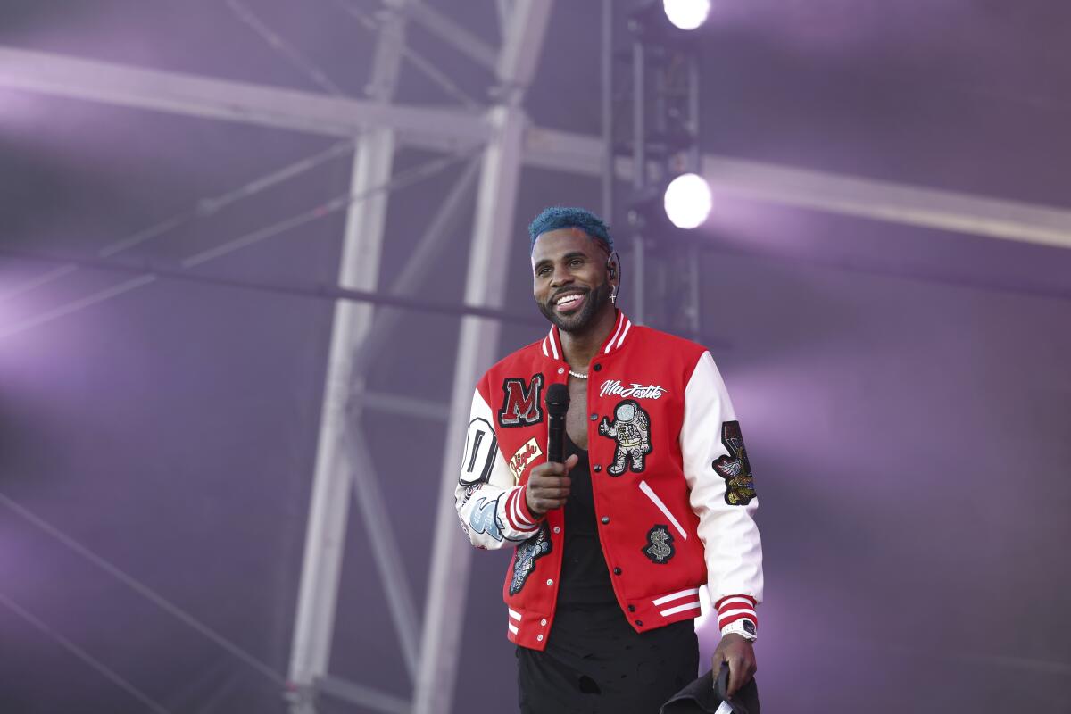 Jason Derulo wears a red and white jacket, a black shirt and black pants as he performs onstage
