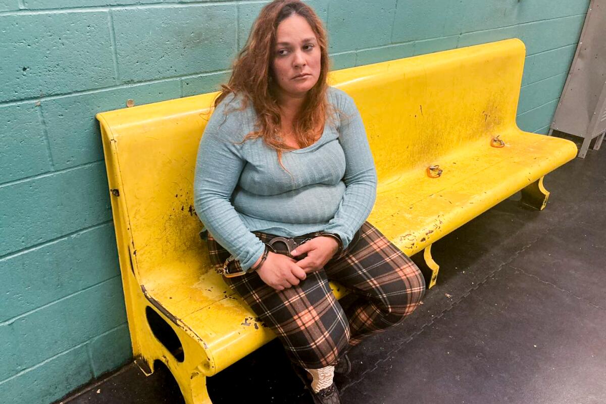 A woman sits on a yellow bench that is against a wall.
