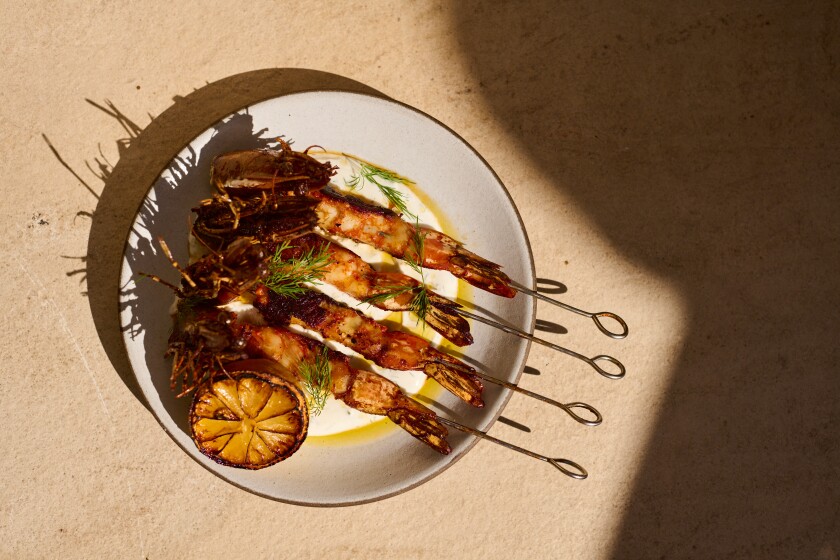 An overhead photo of four prawns, each skewered, served with half a lemon.