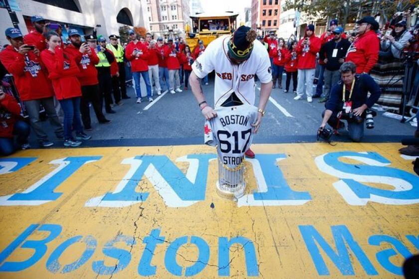 Jonny Gomes of the Boston Red Sox lays the World Series trophy and the 'Boston Strong 617' jersey onto the finish line of the Boston Marathon on Boylston Street during the World Series victory parade.
