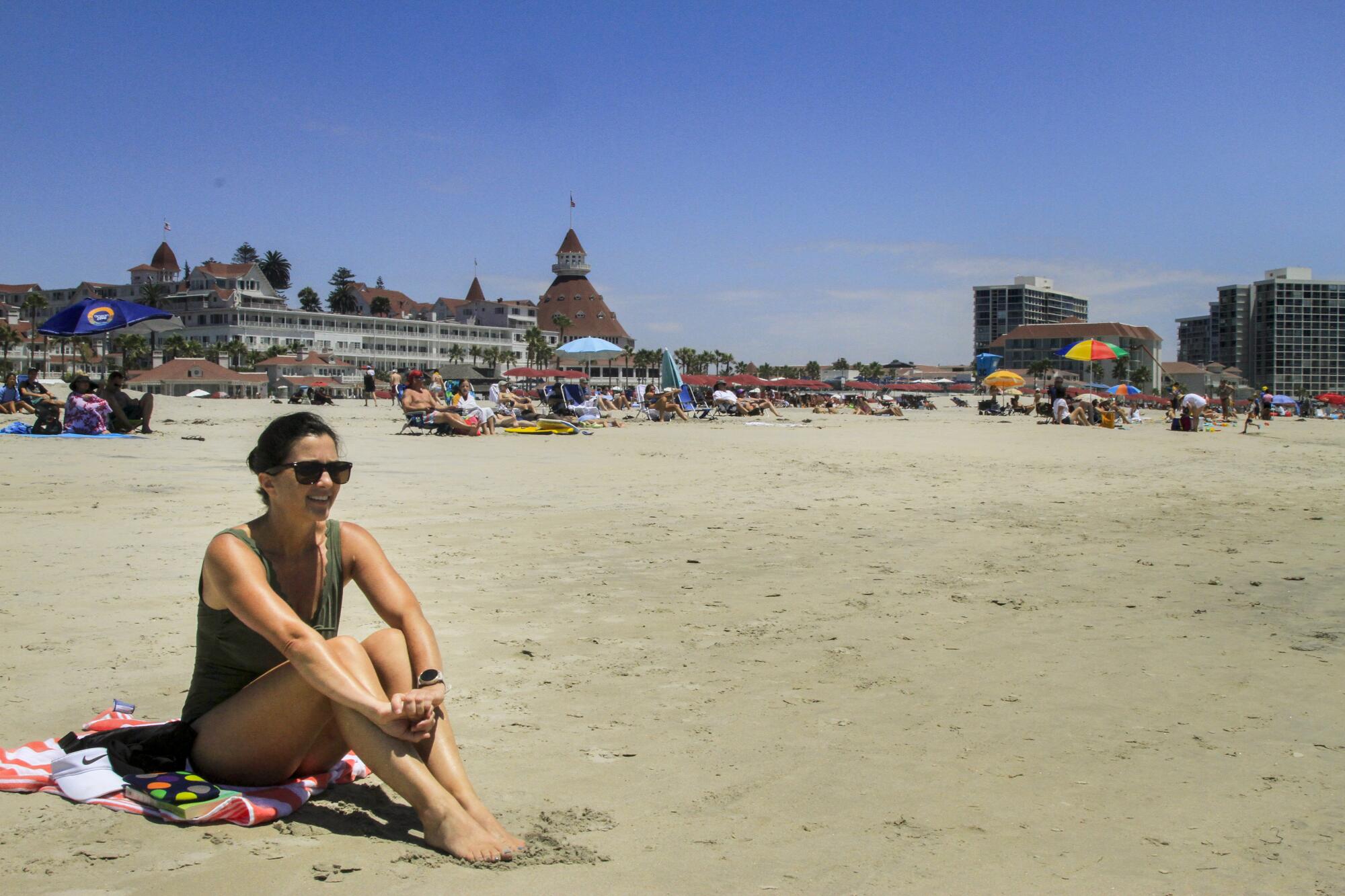 A woman in a bathing suit sits on the beach with the Hotel del Coronado in the background.