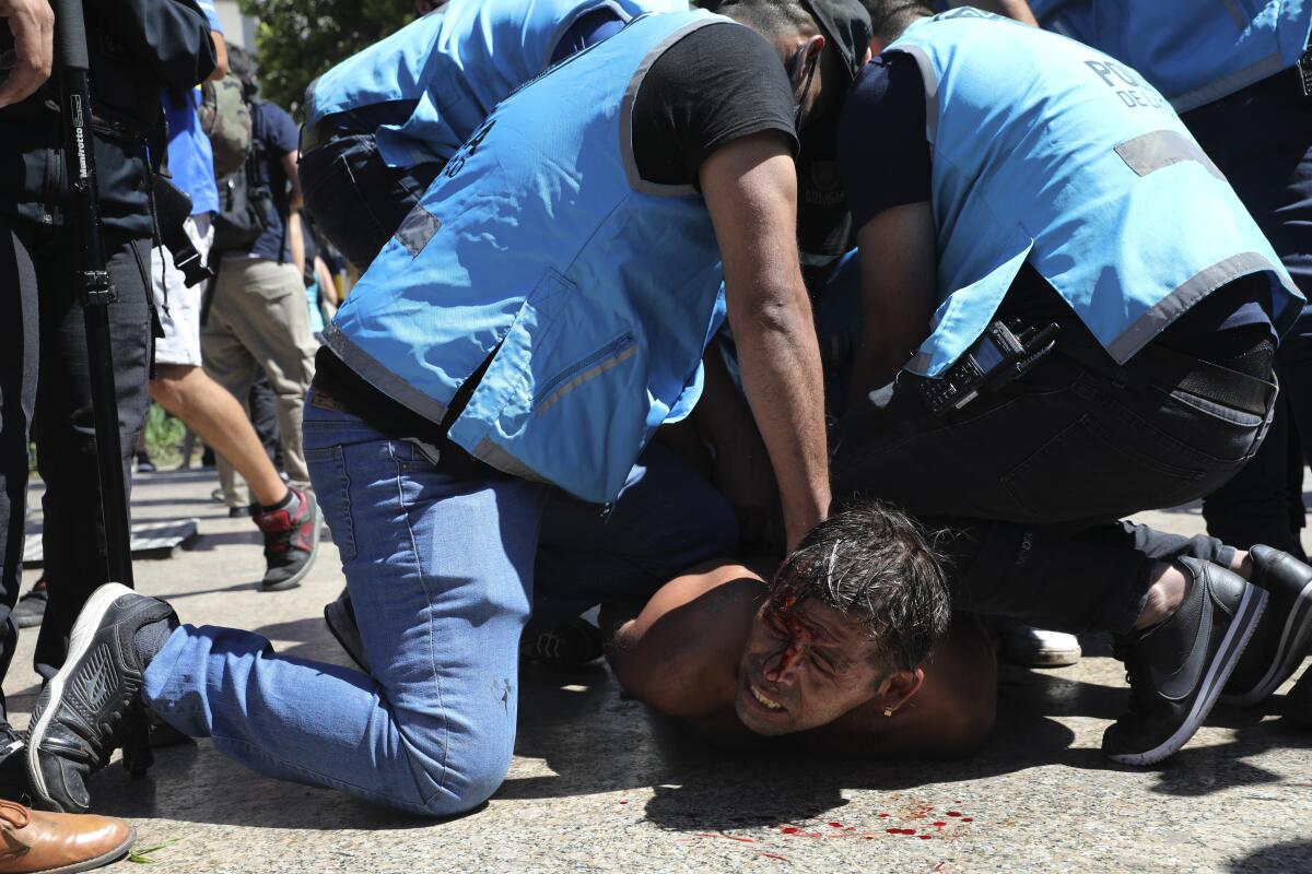 Blood dots the ground and the face of a man as several officers pin him down.