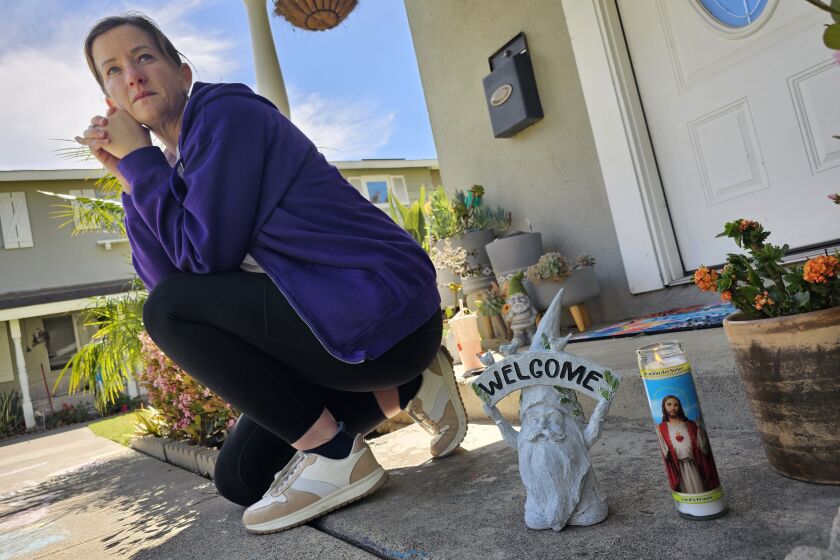 Tori Athey sits next to a garden gnome made by her neighbor, a the victim of a shooting in Huntington Beach Sunday evening.