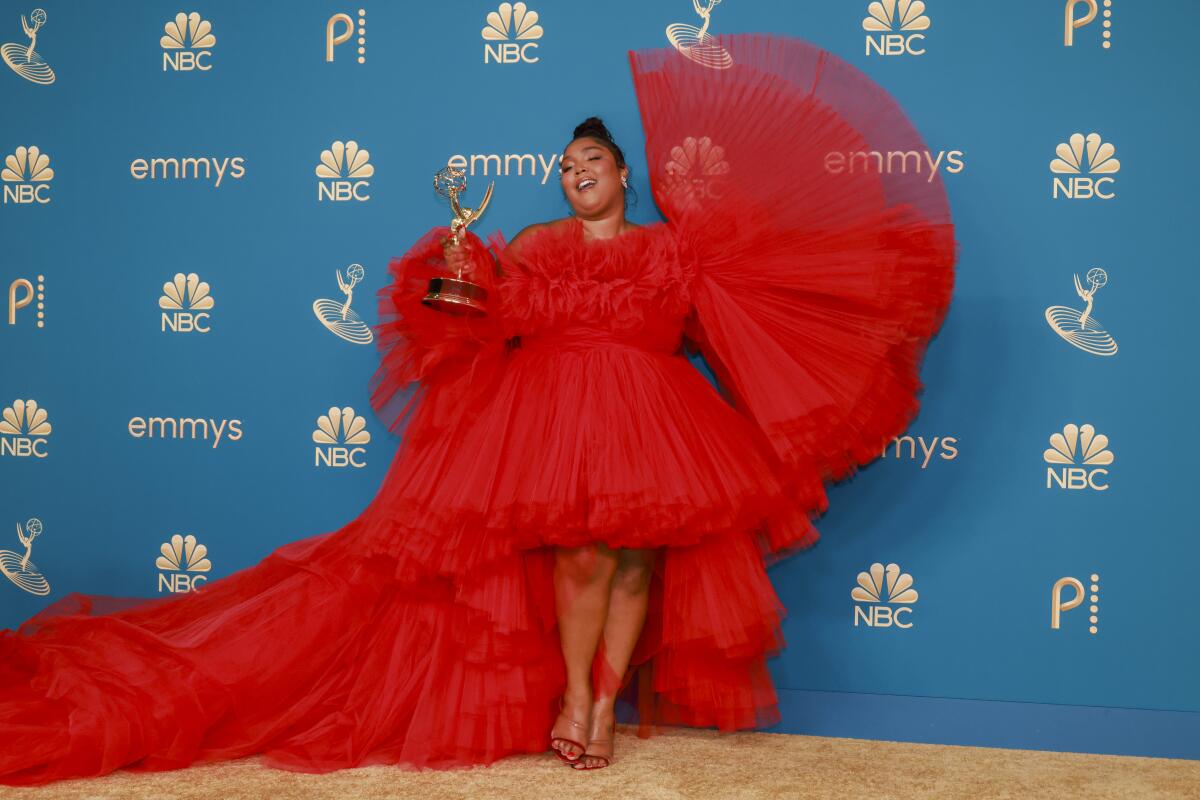 Lizzo raising an arm and her Emmy while wearing a ruffled red dress.