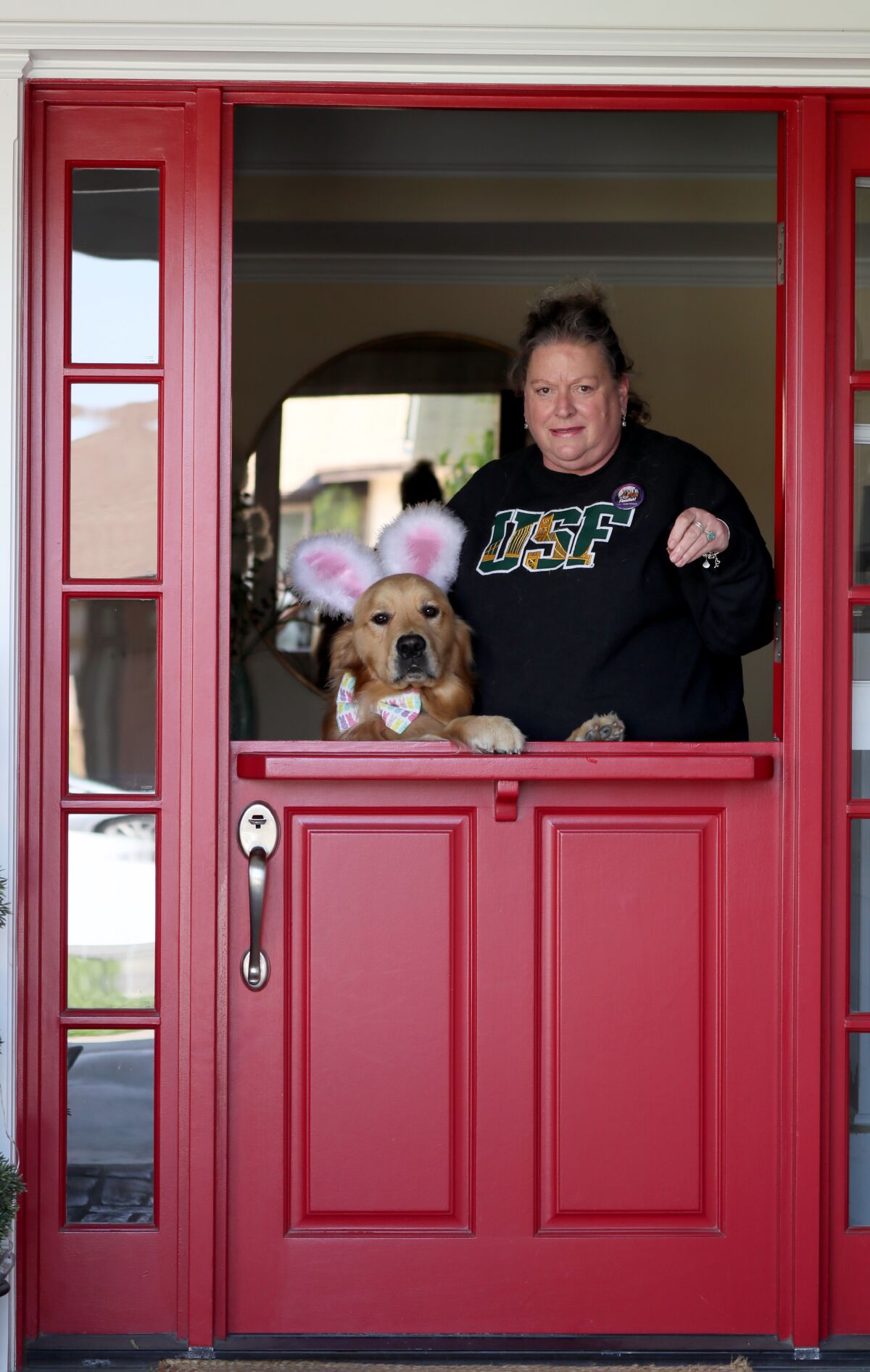 A dog in bunny ears and a woman stand behind a half-door.