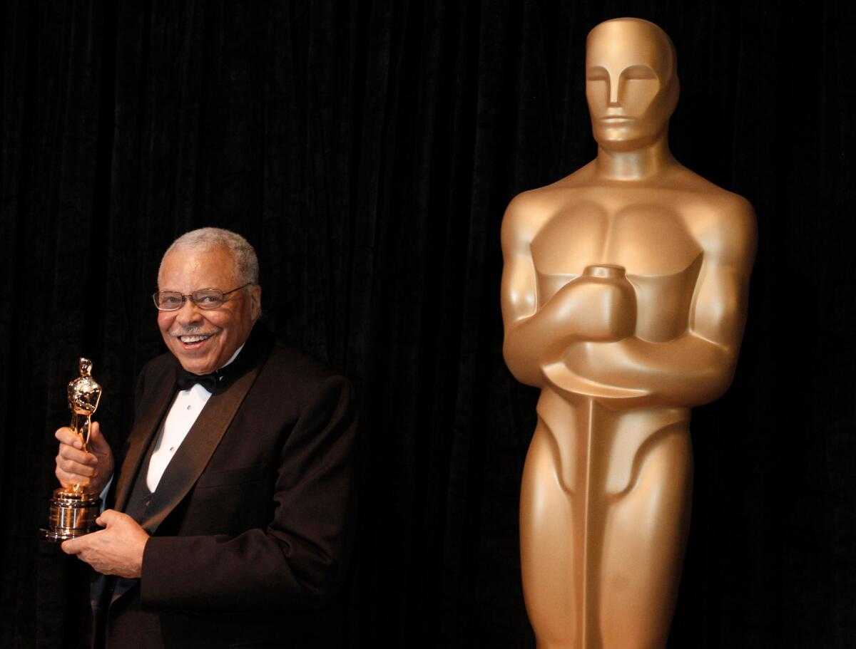 James Earl Jones holding an Oscar statuette and standing next to a large statue of an Academy Award winner 