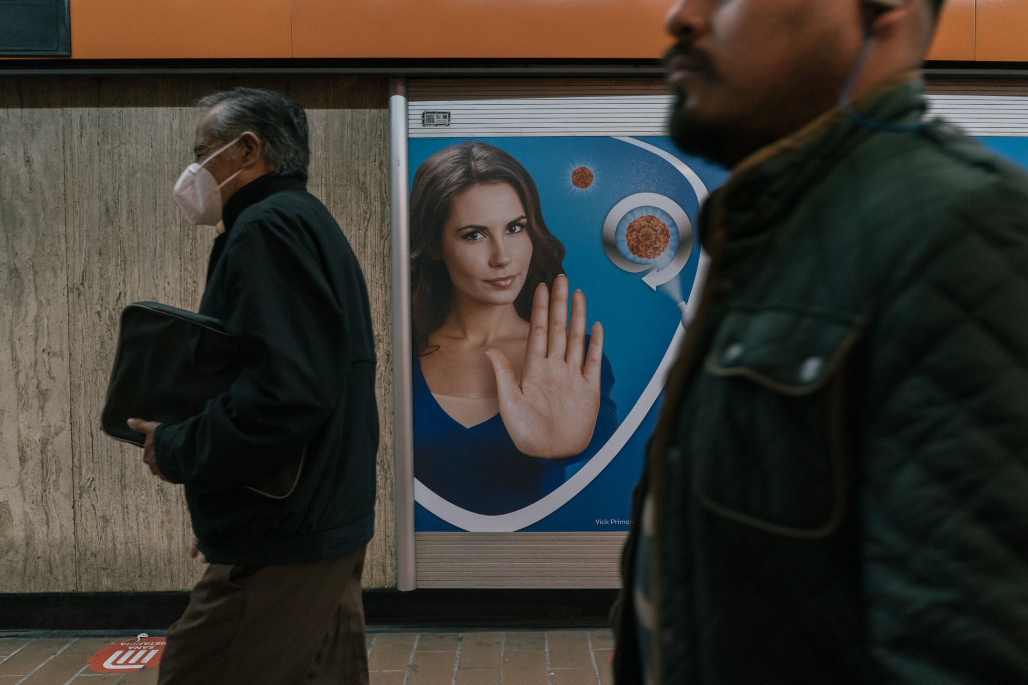 People in the subway in Mexico City pass by an ad picturing a light-skinned woman holding out her hand.