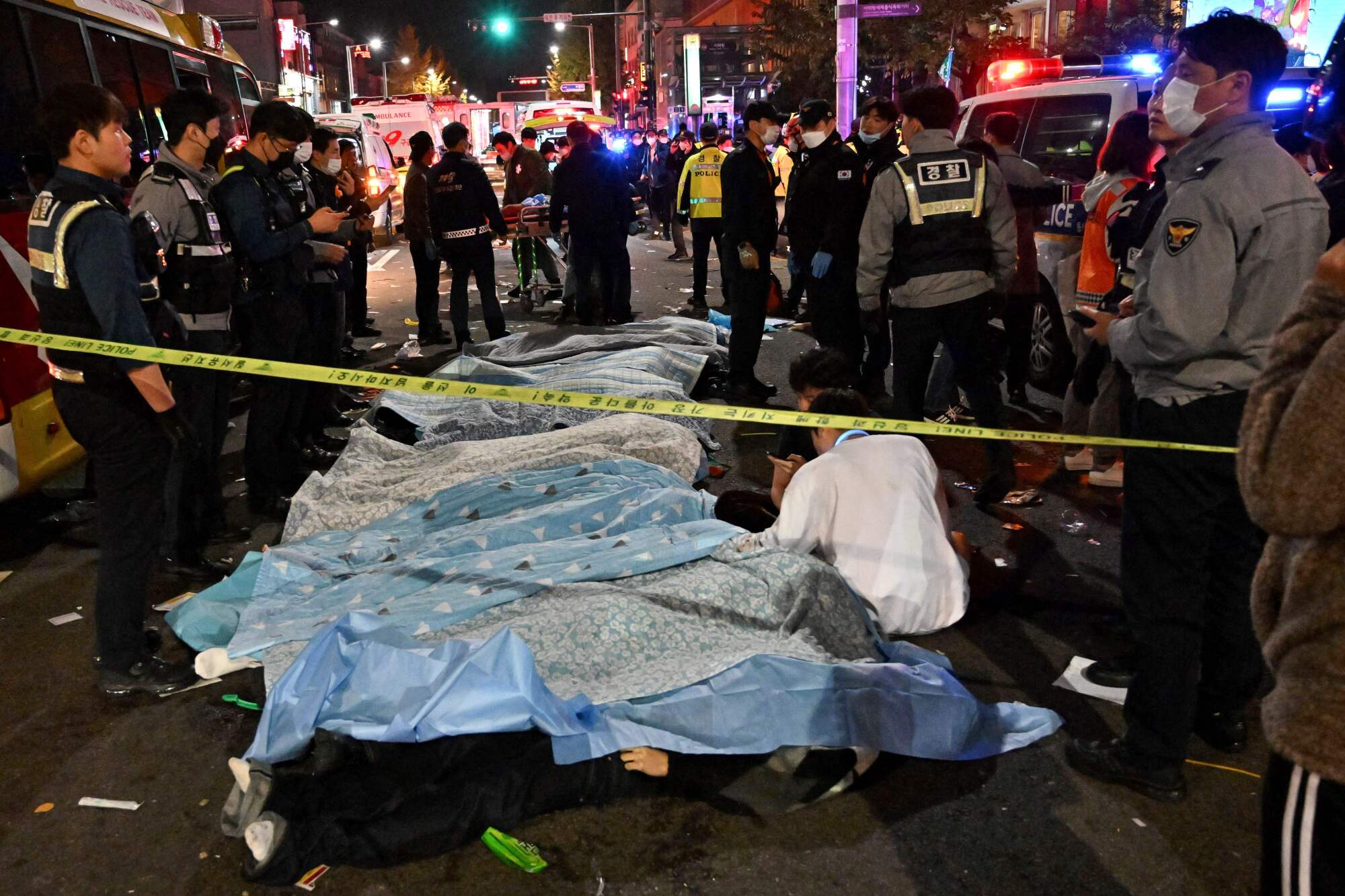 Bodies covered in sheets on a street, surrounded by emergency workers 