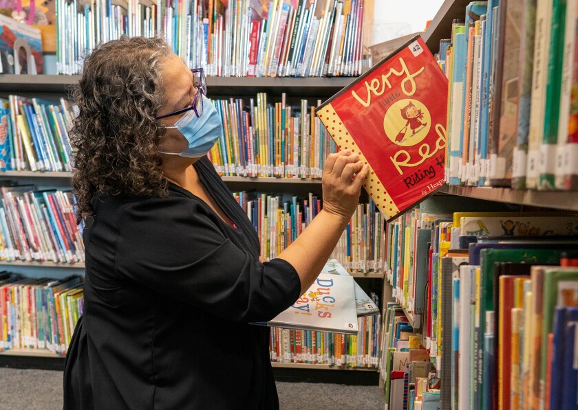 Una mujer saca un libro de un estante de la biblioteca en una sucursal de la Biblioteca Pública de Los Ángeles.