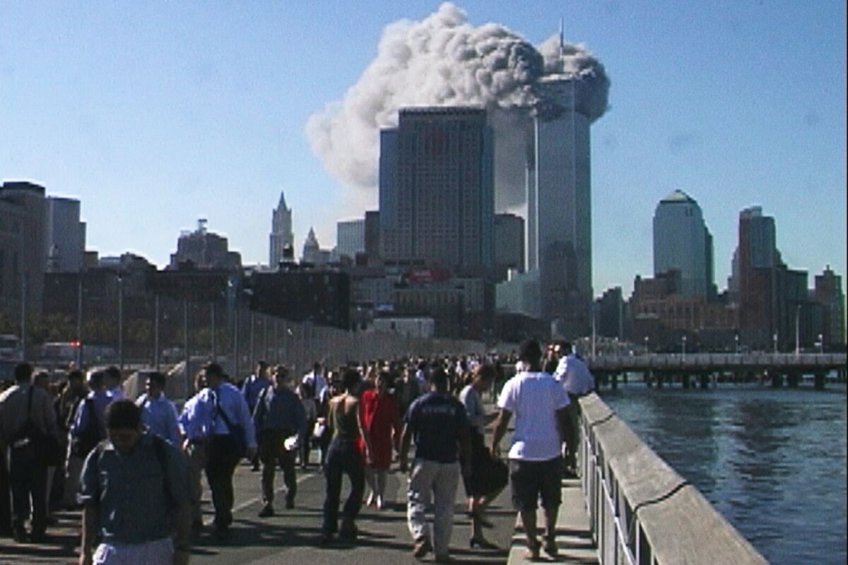 People walk alongside a river as the Twin Towers burn in front of them on Sept. 11, 2001.