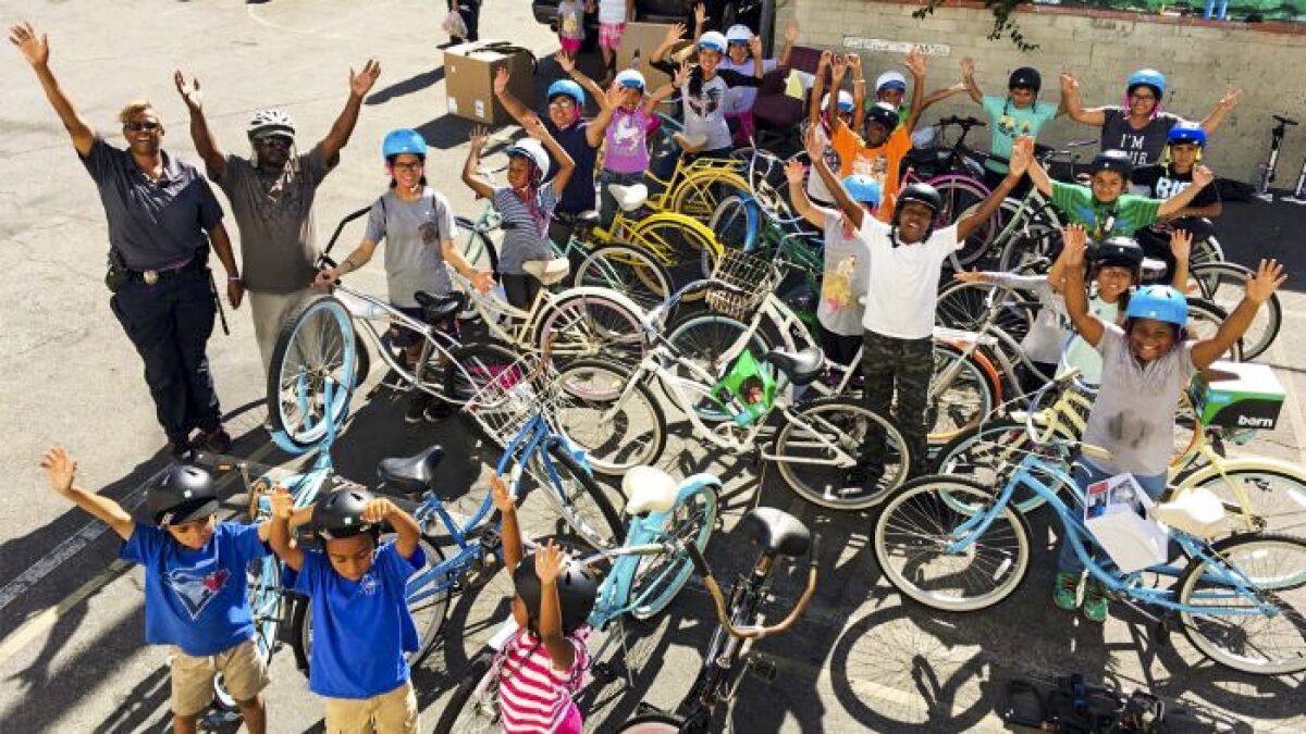 A group of people surround bicycles, raise their hands and smile