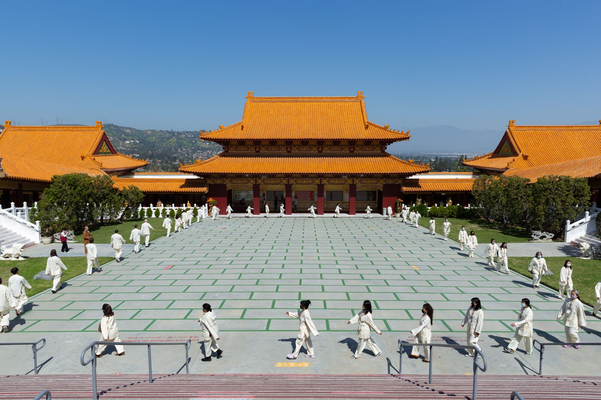 An overhead photo of a temple courtyard with people in white uniforms walking in a square formation