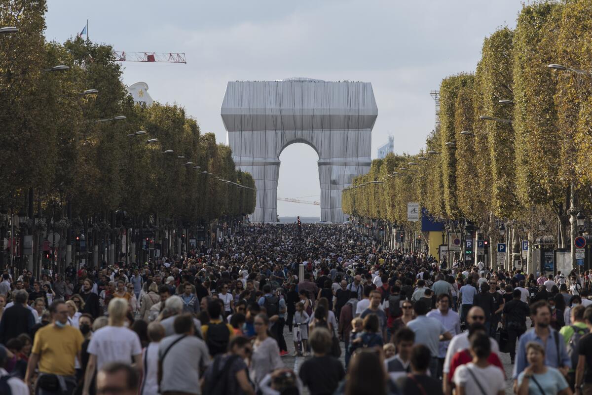 The Arc de Triomphe is seen in a silvery wrap at the end of a road filled with people.