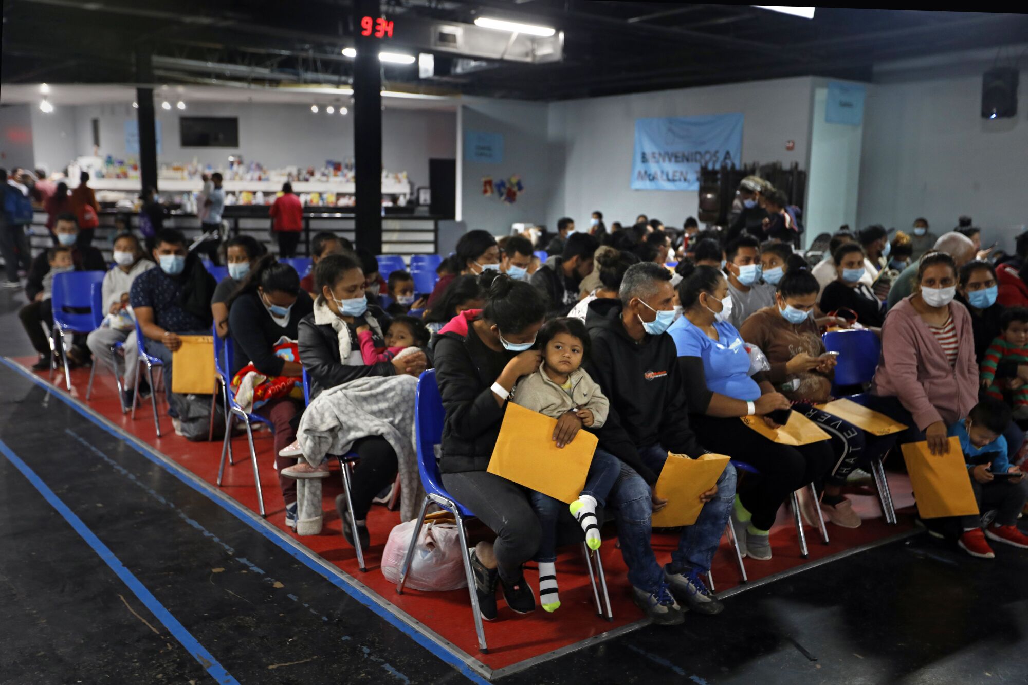 Asylum seekers holding manila envelopes sit in rows of chairs