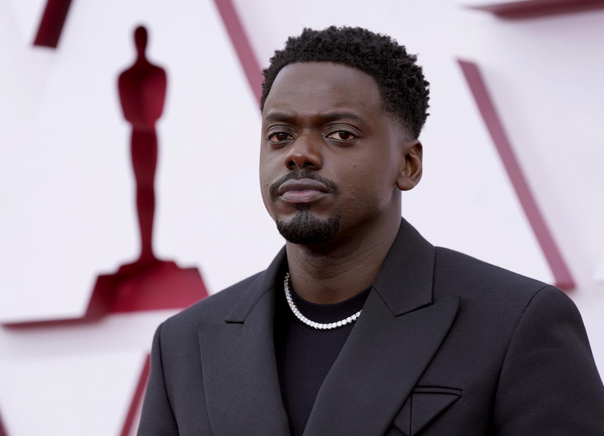 Daniel Kaluuya in a black jacket over a black shirt with a white necklace
