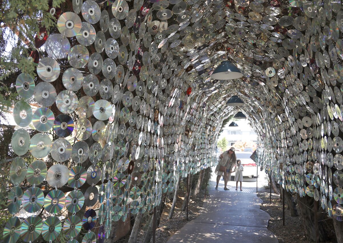 A mother and daughter are at LAB Antimall overlooking a tunnel cut through a bush covered with old music CDs.
