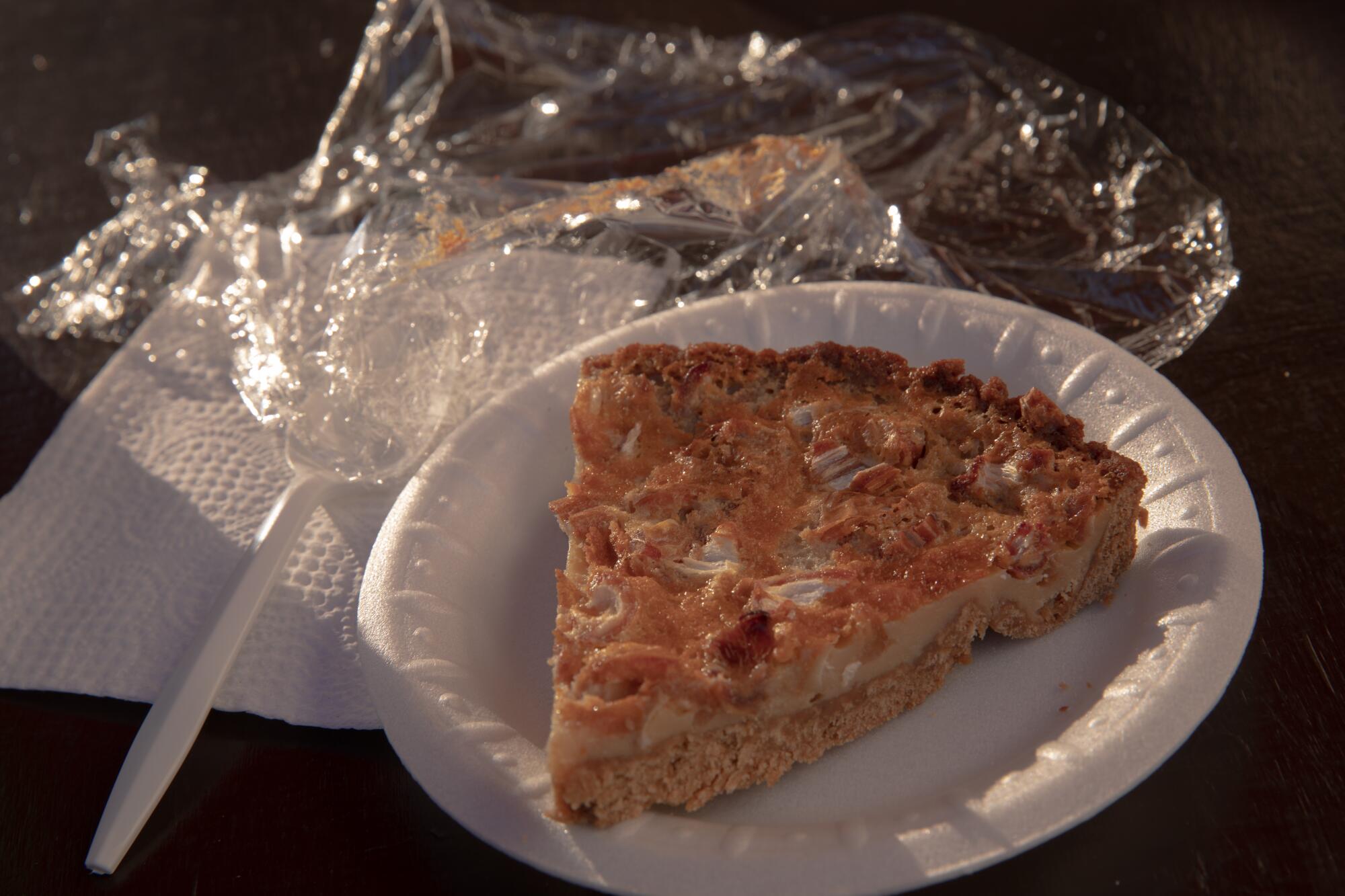 A styrofoam plate holding a slice of fig pie, illuminated by sunlight.