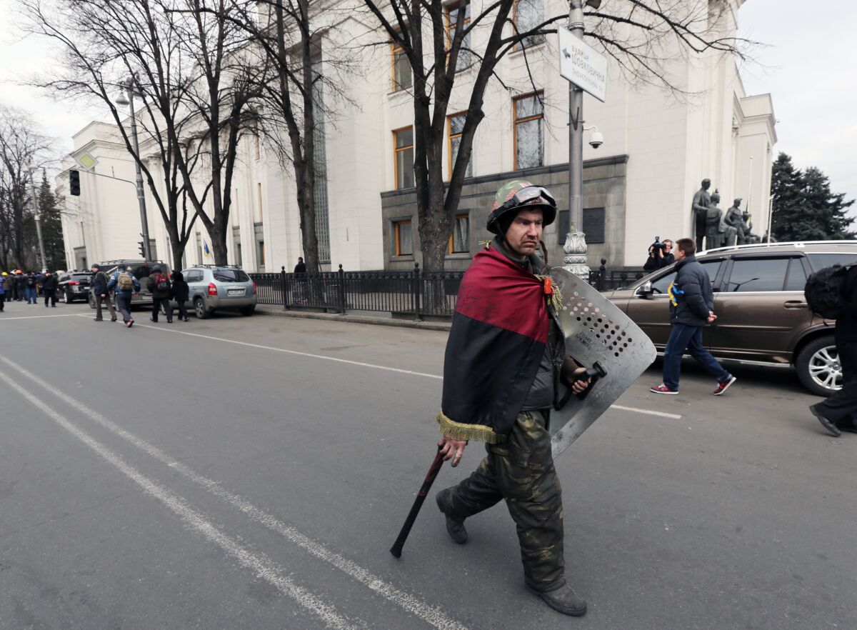 An opposition fighter wrapped in the nationalist red and black flag passes the parliament building in Kiev on Saturday.
