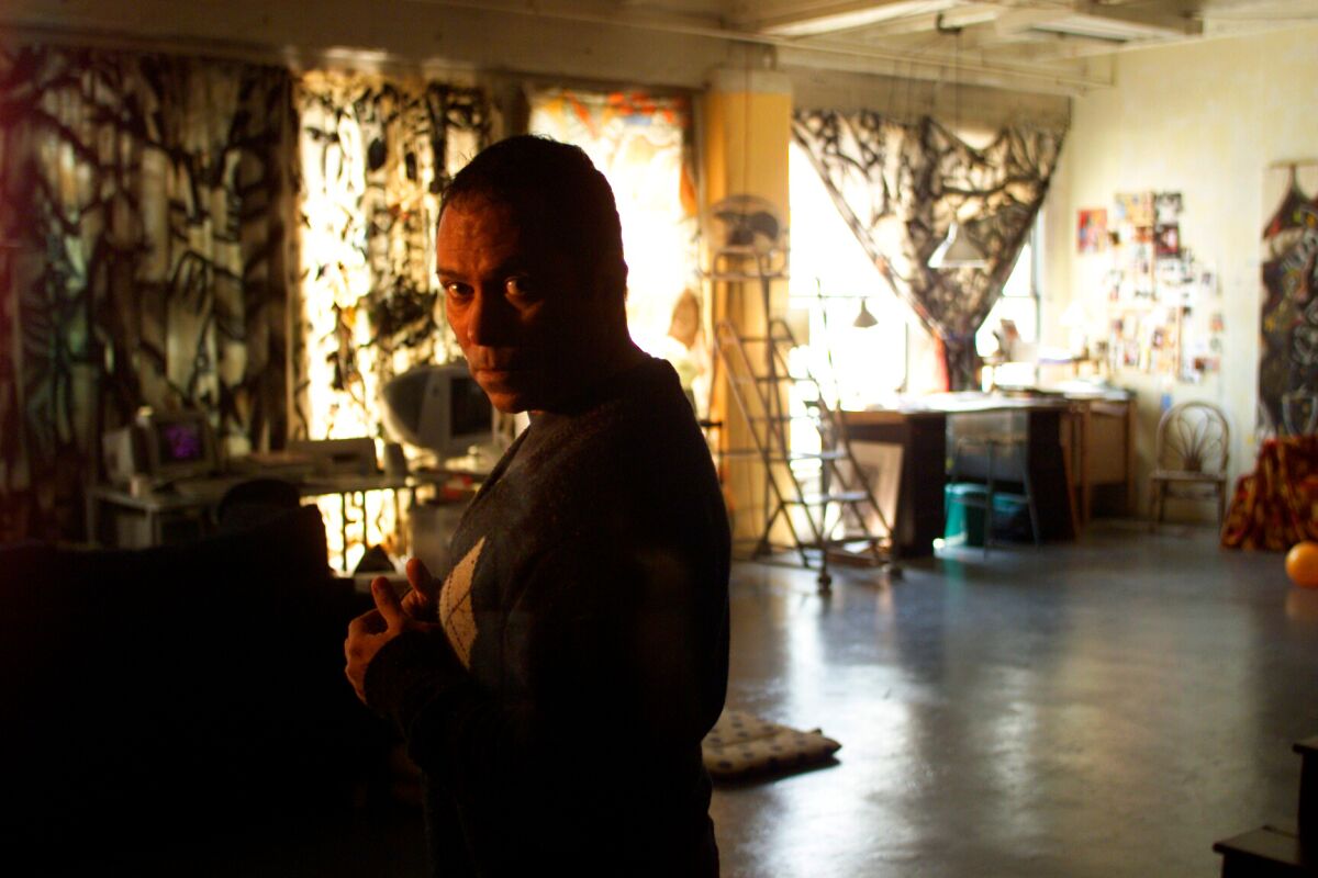 A man stands in shadowy profile in  a large loft with art objects and supplies