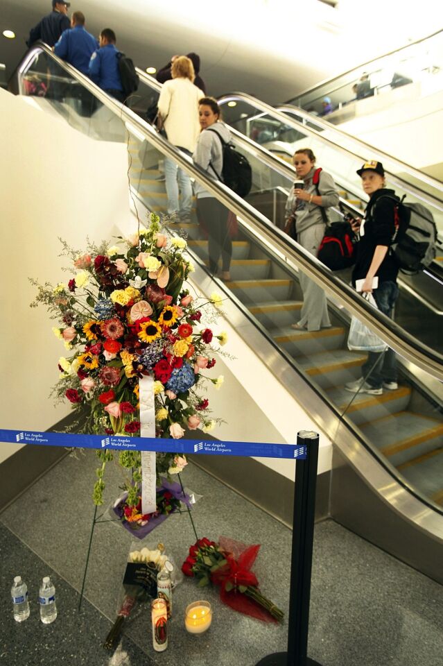Passengers and Transportation Security Administration walk past a memorial of flowers at LAX on Monday morning.