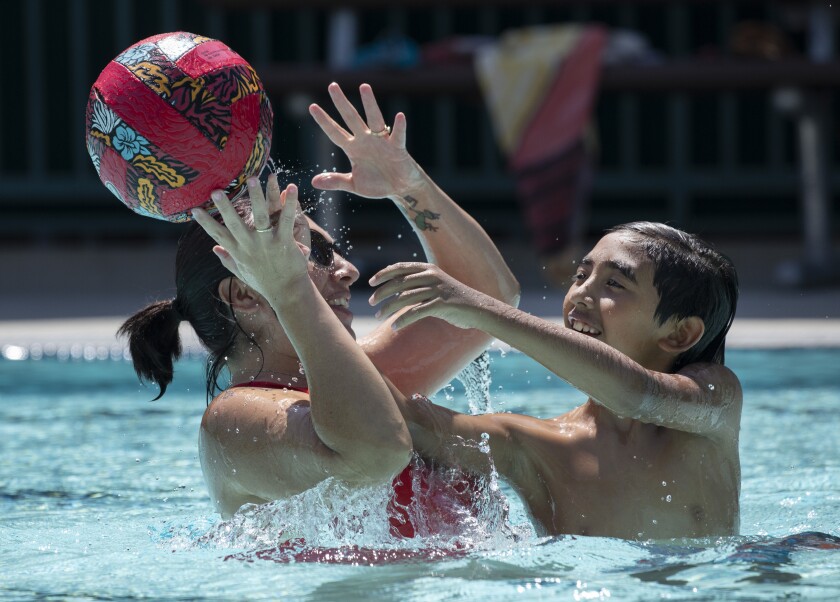 A woman and a boy play with a ball in a pool.