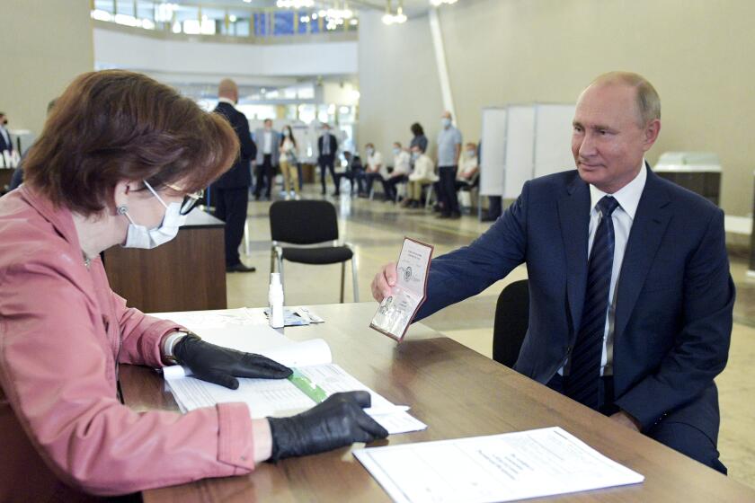 Russian President Vladimir Putin shows his passport to a member of an election commission as he arrives to take part in voting at a polling station in Moscow, Russia, Wednesday, July 1, 2020. The vote on the constitutional amendments that would reset the clock on Russian President Vladimir Putin's tenure and enable him to serve two more six-year terms is set to wrap up Wednesday. (Alexei Druzhinin, Sputnik, Kremlin Pool Photo via AP)