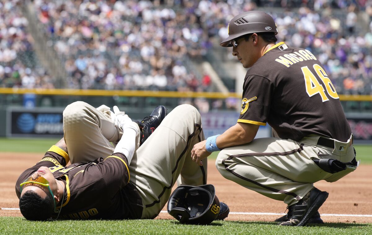 Manny Machado grabs his left ankle after he was injured Sunday. Padres first base coach David Macias looks to help.