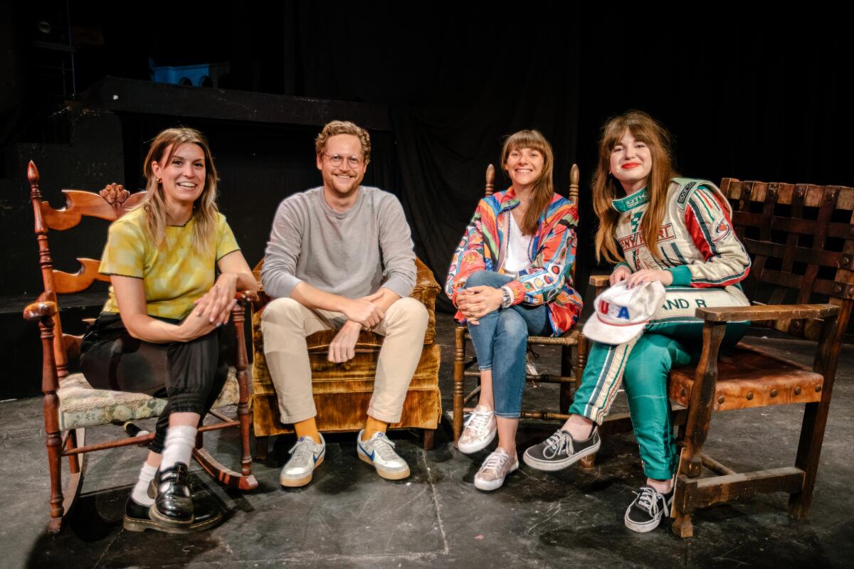 Four people sit in chairs on a stage