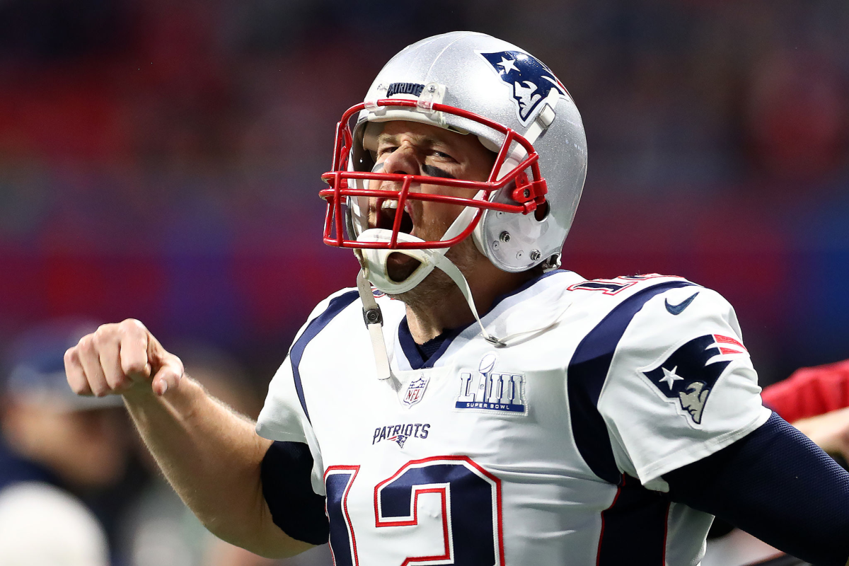 Tom Brady in a New England Patriots uniform pumps his fist running onto the field.