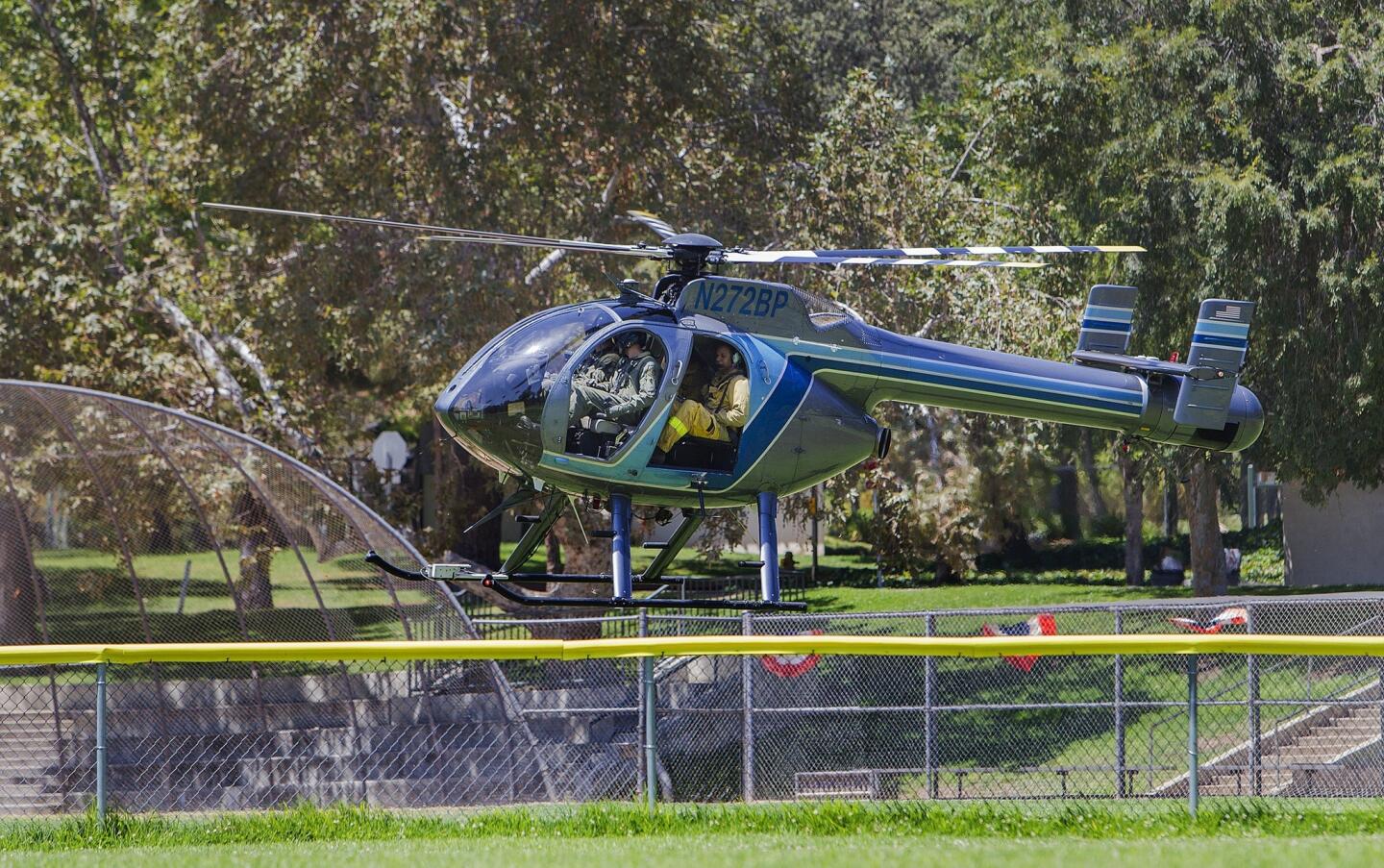 A Glendale police helicopter with two firefighters on board flies over a baseball field en route to the burn area above Brand Park to investigate the suspicious origin of a 150-acre wildfire.