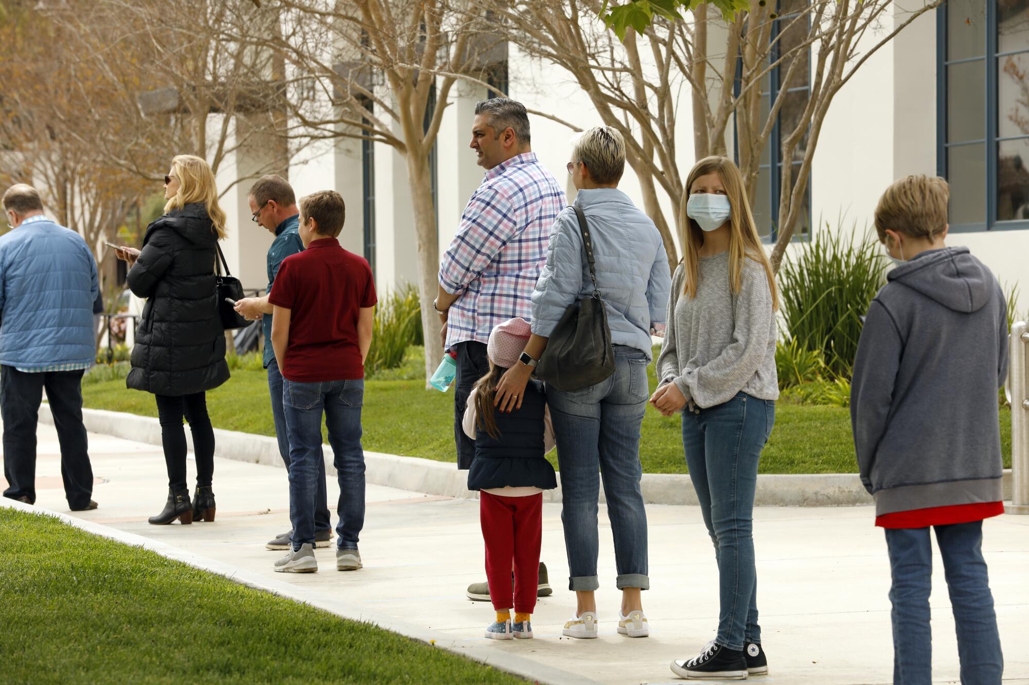 Practicando el distanciamiento social y el uso de mascarillas y guantes, las personas esperan en la fila para comulgar en Godspeak Calvary Chapel en Thousand Oaks.