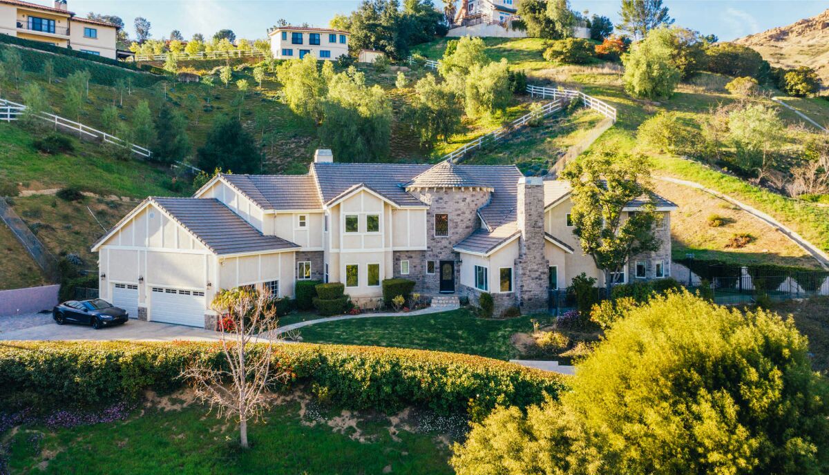 A view of a large traditional-style home amid hills, with brick accents, a turret and a fireplace.