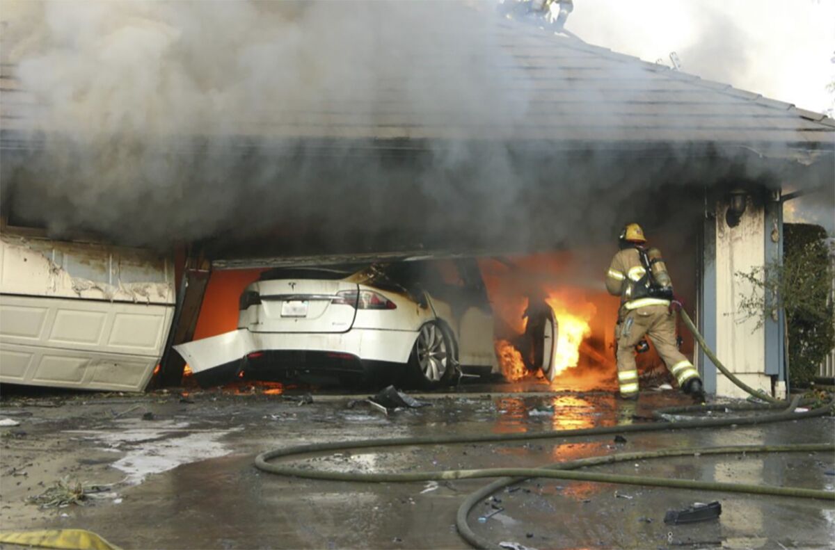 This undated photo provided by National Transportation Safety Board, The Orange County Fire Authority battles a fire on a burning vehicle inside a garage in Orange County, Calif. When firefighters removed the SUV from the garage to assess the fire , they identified the fuel source as the SUV’s high-voltage battery pack. U.S. safety investigators say electric vehicle fires pose risks to first responders, and manufacturers have inadequate guidelines to keep them safe. (Orange County Sheriff’s Department/National Transportation Safety Board via AP)
