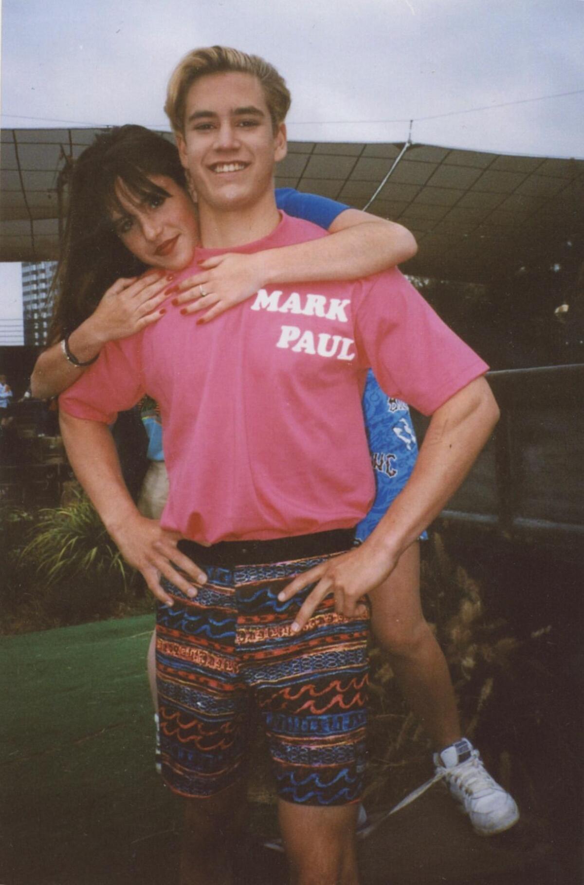 A girl in a blue shirt climbing on the back of a boy in a pink shirt reading Mark Paul