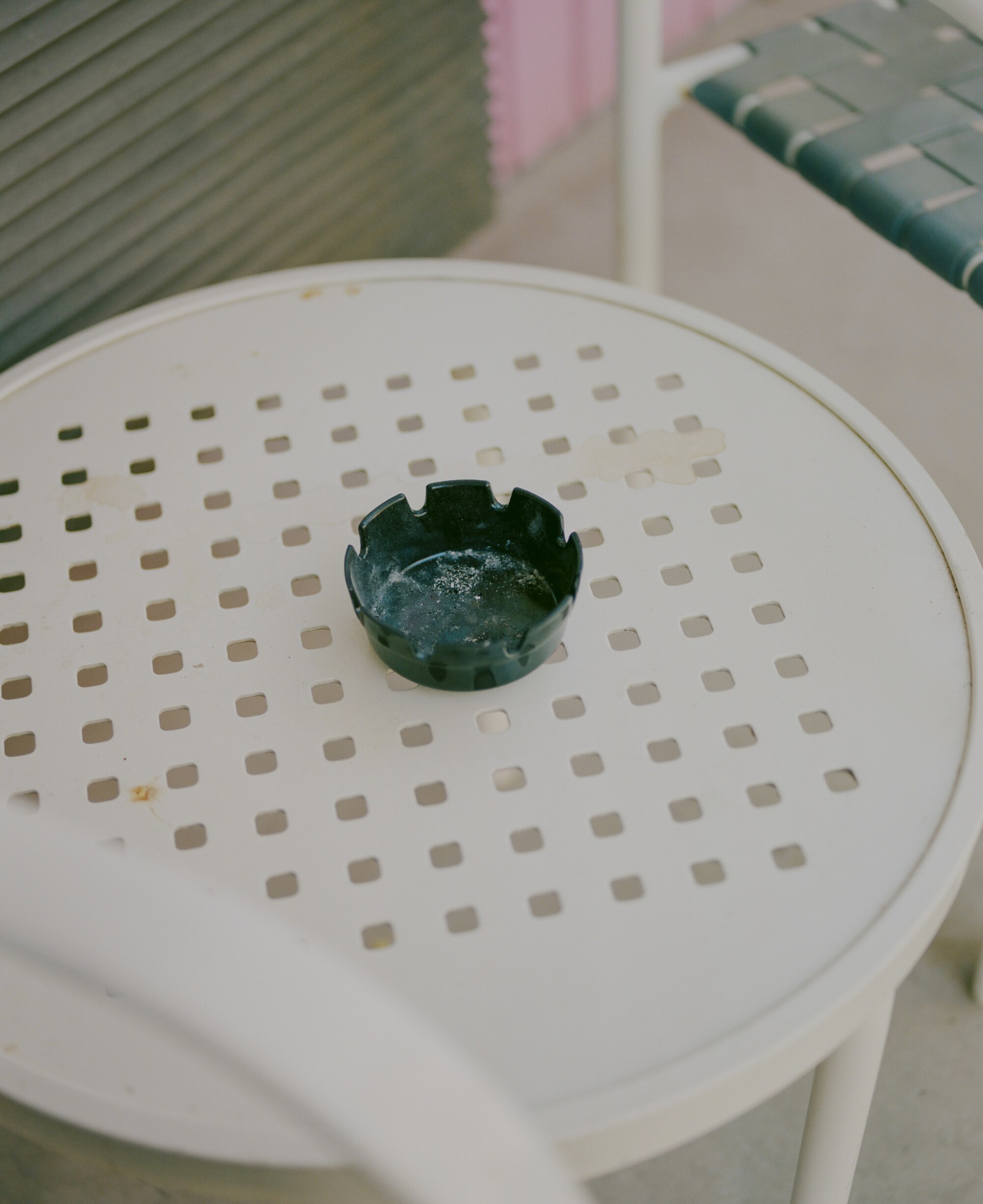 A black ashtray rests on a white table with a perforated top.