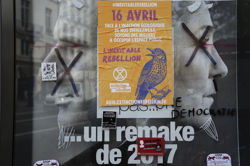FILE - A torn front page ad shows incubent President Emmanuel Macron and challenger Marine Le Pen as the environmental group Extinction Rebellion takes part in a three-day demonstration against what they call France's inaction on climate issues, in the district of Porte de Saint Denis in the center of Paris, France, Monday, April 18, 2022. French President Emmanuel Macron is in pole position to win reelection Sunday, April 24, 2022 in France's presidential runoff. Yet his lead over far-right rival Marine Le Pen depends on one major uncertainty: voters who decide to stay home. A victory in Sunday’s runoff vote would make Macron the first French president in 20 years to win a second term. (AP Photo/Francois Mori, File)