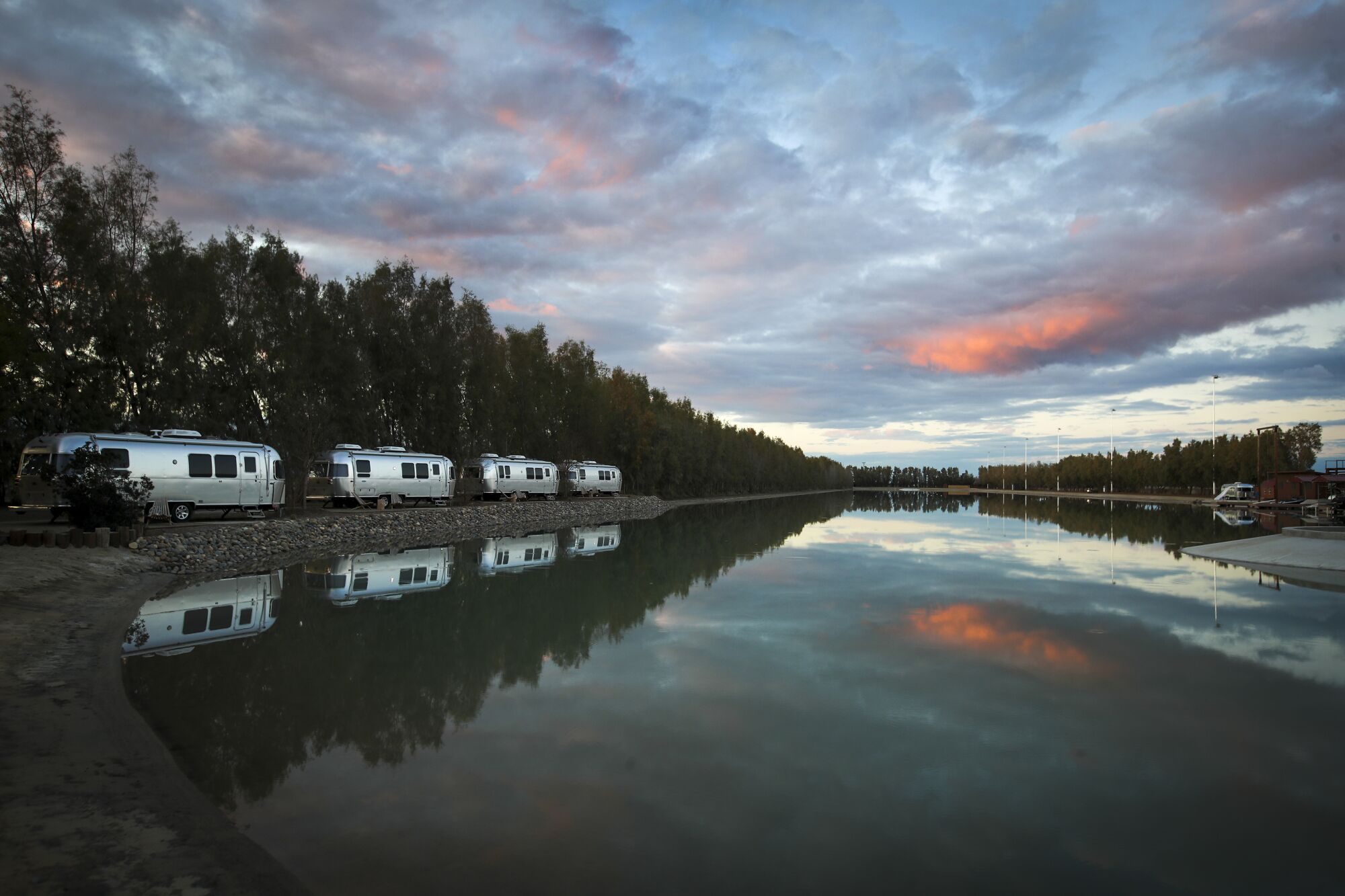 The sun sets over Airstream campers overlooking a lake next to the wave pool