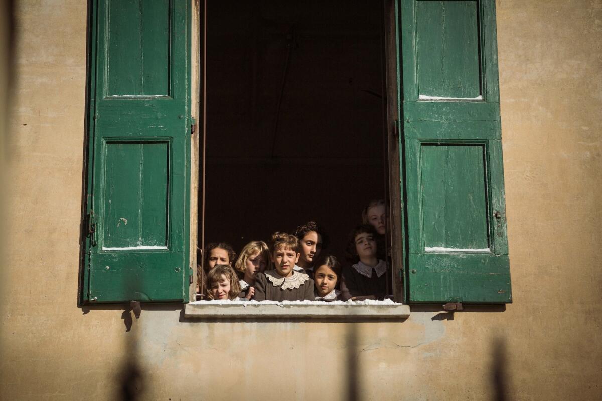 Children look out through an open window with green shutters.