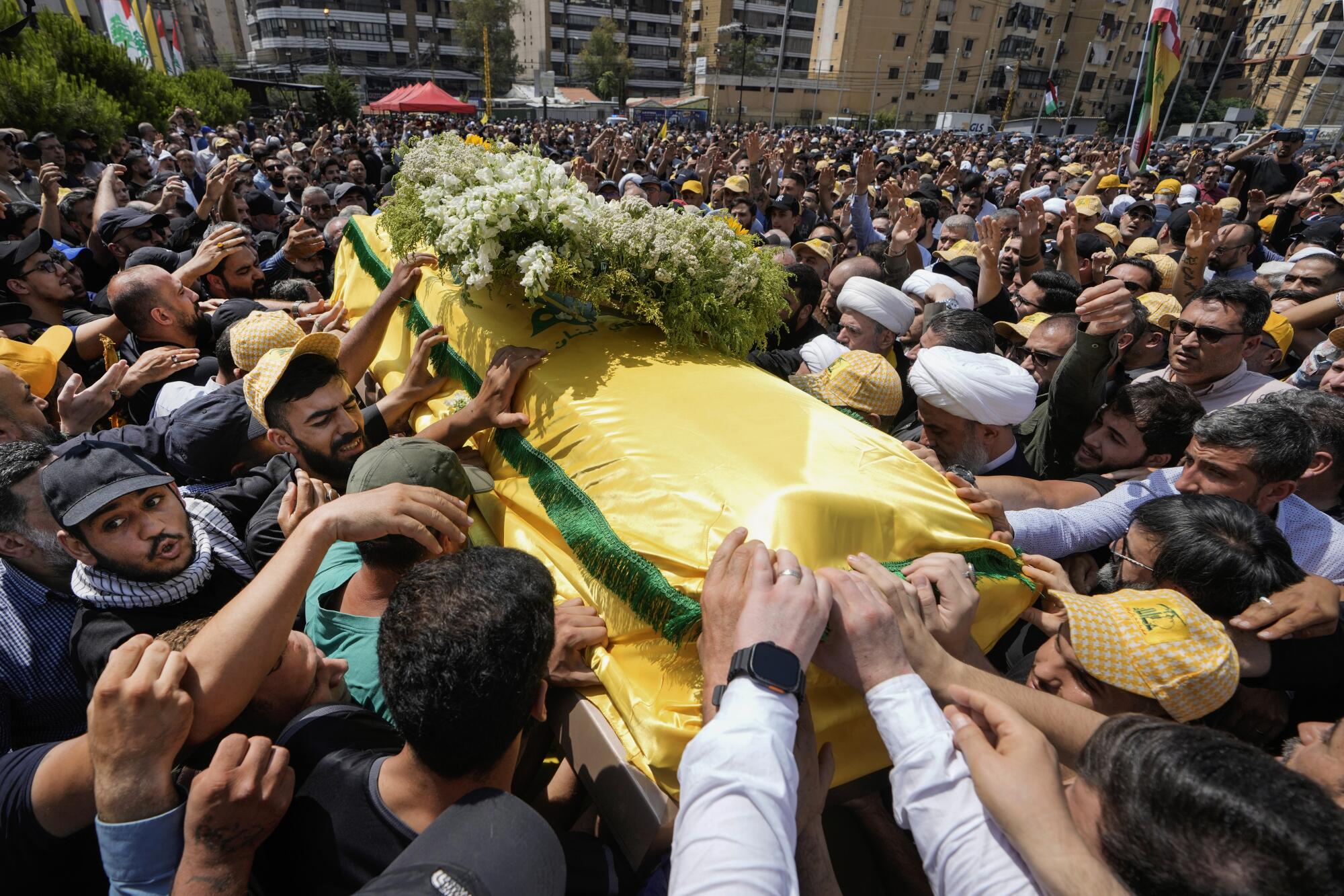 A large crowd surrounds a coffin wrapped in a yellow and green flag, topped with a wreath.